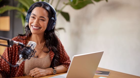 a smiling woman wearing headphones sits in front of a laptop and microphone recording fertility podcast