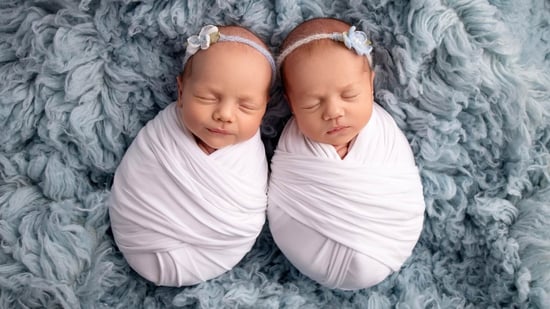 sleeping newborn twin girls swaddled laying on grey blue fluffy blanket