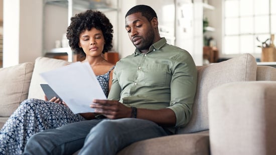 a couple sitting on couch looking at paperwork for insurance