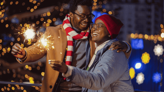 new year's eve happy couple with sparklers in front of holiday lights