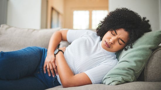 woman laying on couch holding stomach with closed worried eyes