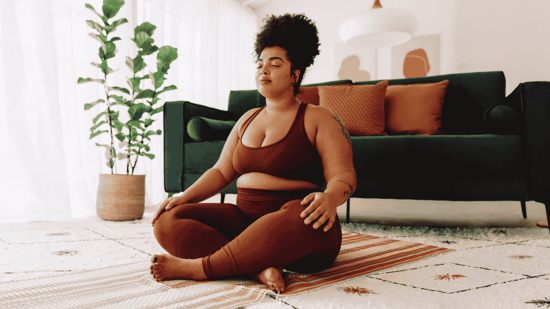 a woman sits cross legged on the floor of her home eyes closed fertility yoga