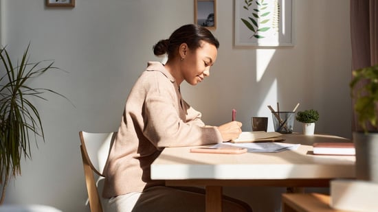 a woman sits at her desk writing in a gratitude journal