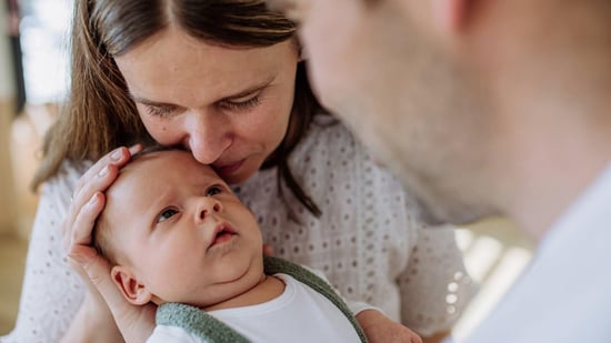 new parents holding newborn baby with mother kissing baby on forehead