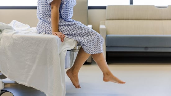 female patient sitting on edge of exam room bed in hospital gown