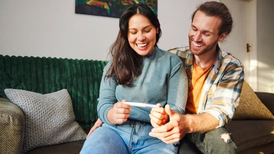 iui vs ivf happy couple holding positive pregnancy test smiling sitting on couch together