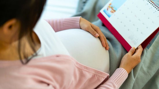 woman holding pregnant belly looking at calendar to calculate due date of baby