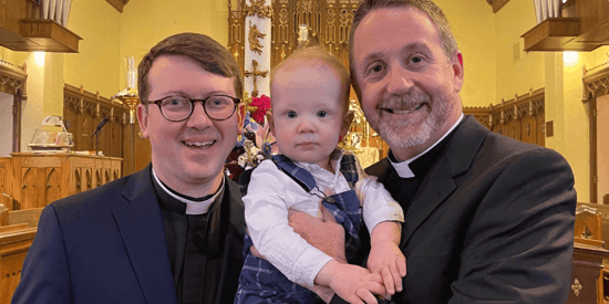 two gay fathers holding their infant son in church