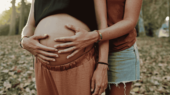 lesbian couple holding pregnant belly outdoors pregnancy photoshoot 