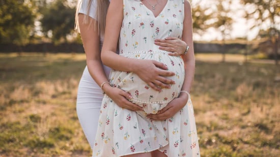 lesbian couple wearing white dresses outdoor pregnancy announcement photoshoot 