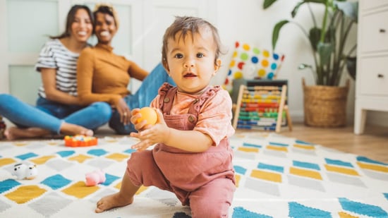 lgbtq lesbian couple sitting on colorful rug with baby in foreground playing