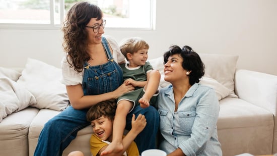 lgbtq family two moms smiling sitting on sofa with their young children