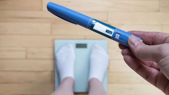 ozempic pen held above weight loss scale