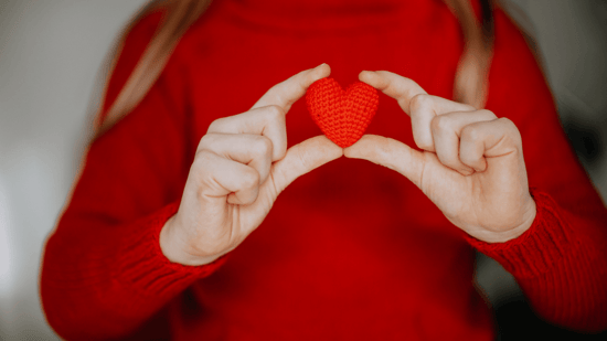 woman in red sweater holding knitted red heart in hands