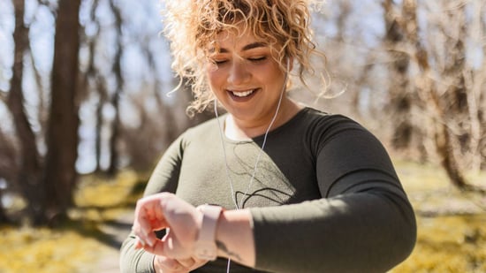 plus size woman with curly hair looking at smart watch to measure heart rate while exercising outdoors