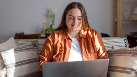 plus size woman sitting on couch smiling down at laptop