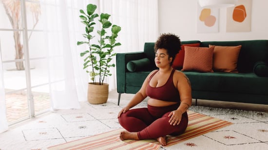 plus size black woman sitting cross-legged on yoga mat at home with eyes closed