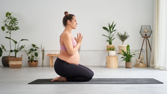 pregnant woman on yoga mat eyes closed on knees