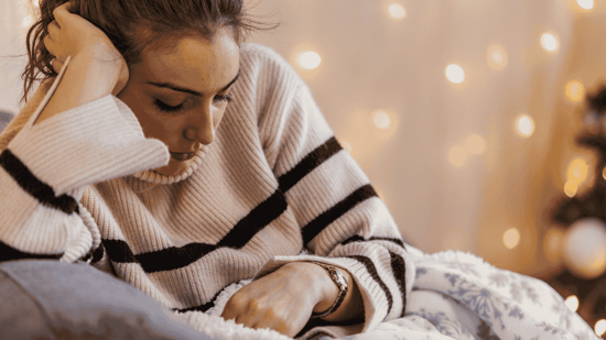 sad woman sitting on sofa with christmas lights behind her